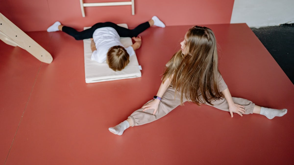 Two children engaging in gymnastics on a mat indoors, showcasing flexibility and playfulness.